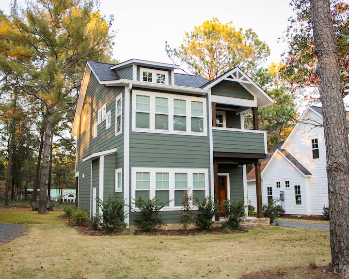 So Pines Cottage, a green two-story home surrounded by pine trees