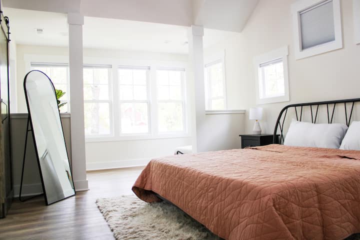 King bedroom with large windows and a quilted terracotta bedspread